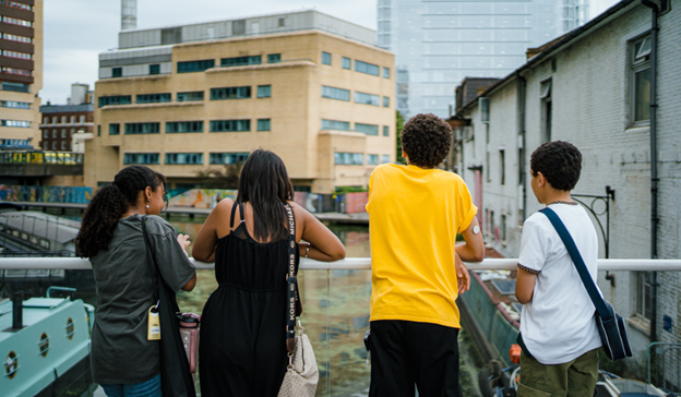 Photograph of four adolescents standing with their back to the camera. St Mary's Hospital, Paddington can be seen in the background behind them.