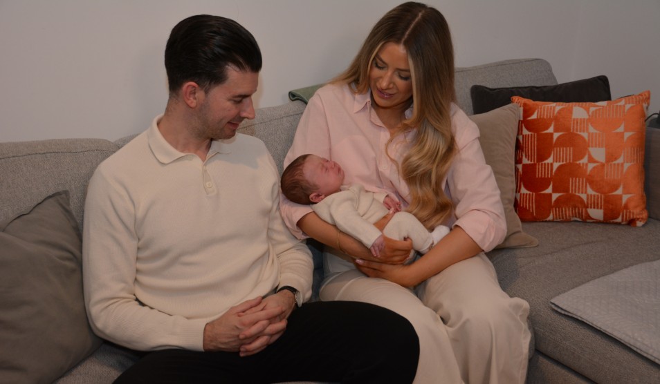 Photo of Steve and Grace sitting on a sofa holding baby Hugo