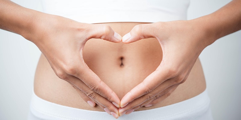 A woman holds her hands over her stomach in a heart shape